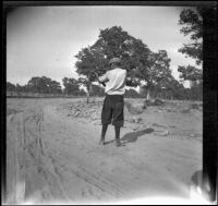 Wilfrid Cline, Jr. aiming his rifle while standing in a dirt road, Redding vicinity, 1917