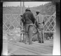 Harry Schmitz and Wilfrid Cline, Jr. stand on a bridge and look down at Fall River, Shasta County, 1917