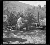 Albert Schmitz crouching next to the camp stove, June Lake vicinity, 1914