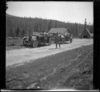 Dave F. Smith standing by the cars near a log cabin in Phillips, Eldorado National Forest, 1913