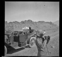 Nella West reads a newspaper and Mary A. West uses binoculars during a stop along the road, Owens Lake (Inyo County), 1913