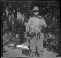 Dave F. Smith posing in camp with the limit of golden trout, Inyo County, 1913