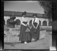 Mary West and Bessie Velzy sit on a fountain across the street from Mission San Fernando Rey de España, Mission Hills, Los Angeles, 1909