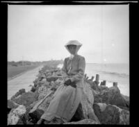 Mary West sits on the rocks with the Hotel del Coronado in the distance, Coronado, 1909