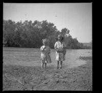 Frances and Elizabeth West stand in water by the muddy shore, Anaheim vicinity?, 1909
