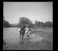 Elizabeth and Frances West stand in the water by the muddy shore, Anaheim vicinity?, 1909