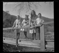 Close-up view of Frances West, Irene Schmitz, Elizabeth West and Chester Schmitz posing while standing on a footbridge, San Francisquito Canyon, about 1914