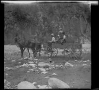 Will P. Mead, Mary A. West, Sena Mead and Paul Mead ford a stream in their wagon, San Gabriel Canyon, about 1903