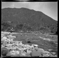 Will P. Mead fishes while perched atop a rock in the San Gabriel River, San Gabriel Canyon, about 1903