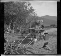 Mary A. West washing dishes alongside the Owens River, Mono County, about 1915