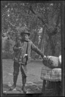 H. H. West poses next to bundled camp bedding, Yosemite National Park, about 1923