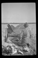 Frank Mellus kneels near Keeper E. D. Hardy as he strings ducks, Seal Beach vicinity, 1916