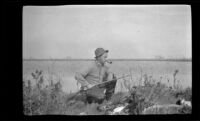 Glen Velzy sitting on an embankment while duck shooting, Seal Beach vicinity, 1917