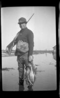 Frank Mellus poses with his rifle and a string of ducks, Seal Beach vicinity, 1920