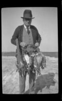 John Masters poses with his rifle and a string of ducks, Seal Beach vicinity, 1920