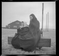 Fannie Mead Biddick and her daughter, Ruth, sit wrapped in a blanket on a bench on the beach, Venice, about 1910