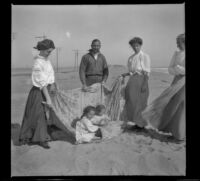 Maude Hamilton, Guy West, and Mary West hold a blanket that Elizabeth and Frances West sit upon while Wilhelmina West stands nearby, Venice, about 1908