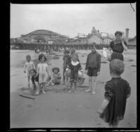 Sena Mead stands while Elizabeth West, Frances West and Paul Mead play on the beach with other children, Venice, about 1910