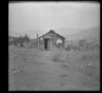 George M. West posing in front of a log cabin (blurry), Yreka, 1898