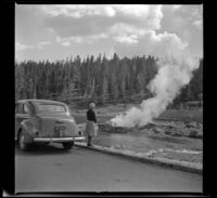 Mertie West watches from the roadside as Riverside Geyser erupts, Yellowstone National Park, 1942