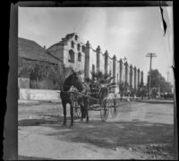 H. H. Cooper rides in a carriage in front of San Gabriel Mission, San Gabriel, about 1900