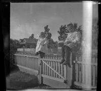 Romayne and Lester Shaw sit on fence posts in the Whitaker's front yard, Los Angeles, about 1900