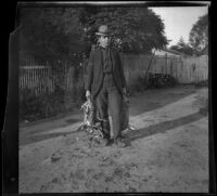 H. H. West stands in his backyard holding rabbits he hunted, Los Angeles, about 1900