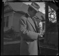 H. H. West stands in front of his house holding a doll, Los Angeles, about 1900