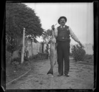George M. West stands in his backyard holding a fish, Los Angeles, 1901