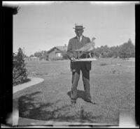 H. H. West stands on his front lawn holding a stuffed bird, Los Angeles, 1917