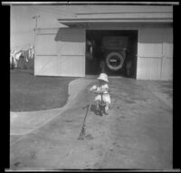 H. H. West Jr. rides his kiddie cart down the driveway, Los Angeles, about 1919