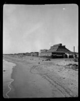 View of a beach lined with beech cottages, 1900-1920