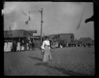 Beach scene with woman looking towards the camera and a crowd strolling along the beach walkway, Los Angeles vicinity, 1898-1915