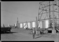 Man walking in fron tof petroleum industry storage tanks, California, 1930-1939