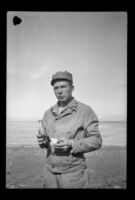 PFC H. H. West, Jr. poses while eating near the shoreline, Aleutian Islands, 1943