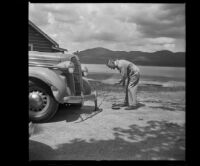 Wayne West fixes a flat tire on his car, Big Bear Lake, 1945
