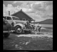 Wayne West fixing a flat tire on his car, Big Bear Lake, 1945