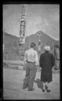 Mertie West and the West's taxi driver look at the totem poles at Saxman Totem Park, Saxman, 1946