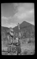 Mertie West poses beside a carved figure at Saxman Totem Park, Saxman, 1946