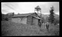 W. L. Kinsell, Frances Wells and Mertie West stand in front of the Old St. Nicholas Russian Orthodox Church at Eklutna Historical Park, Eklutna, 1946