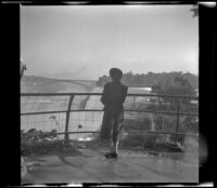 Mertie West stands behind a guardrail and looks towards American Falls, Niagara Falls, 1947