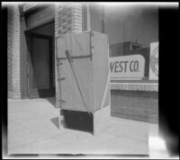 Woodlin electric refrigerator, covered in packaging, stands on a sidewalk, Los Angeles, 1948