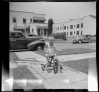 Tommie Newquist rides his tricycle along a walkway, Los Angeles, 1948