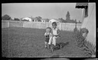 Bobby and Billy Burgess play on a tricycle in their yard, Bell Gardens, 1948
