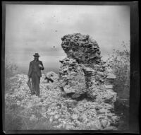 Man in a suit and hat standing among ruins, Turkey, 1895