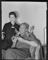Charley "Red" Ruffing, New York Yankees pitcher, and his wife, Pauline Ruffing, holding trophies in their house, Long Beach, 1939