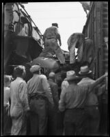 Spectators watch as rescuers climb atop a car wedged between 2 train cars, [between 1920-1939]