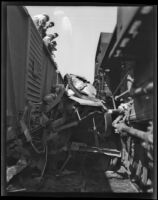 Automobile's mangled remains lie between 2 train cars, [between 1920-1939]