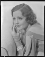 Nancy Carroll, actress, in a salon in front of a fireplace, circa 1933-1935