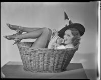 Inez Courtney, actress, in a basket wearing a witch's hat and holding an apple, circa 1934-1939
